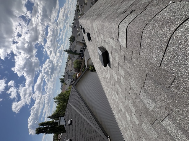 Grey shingle roof with a roof vent, clouds above