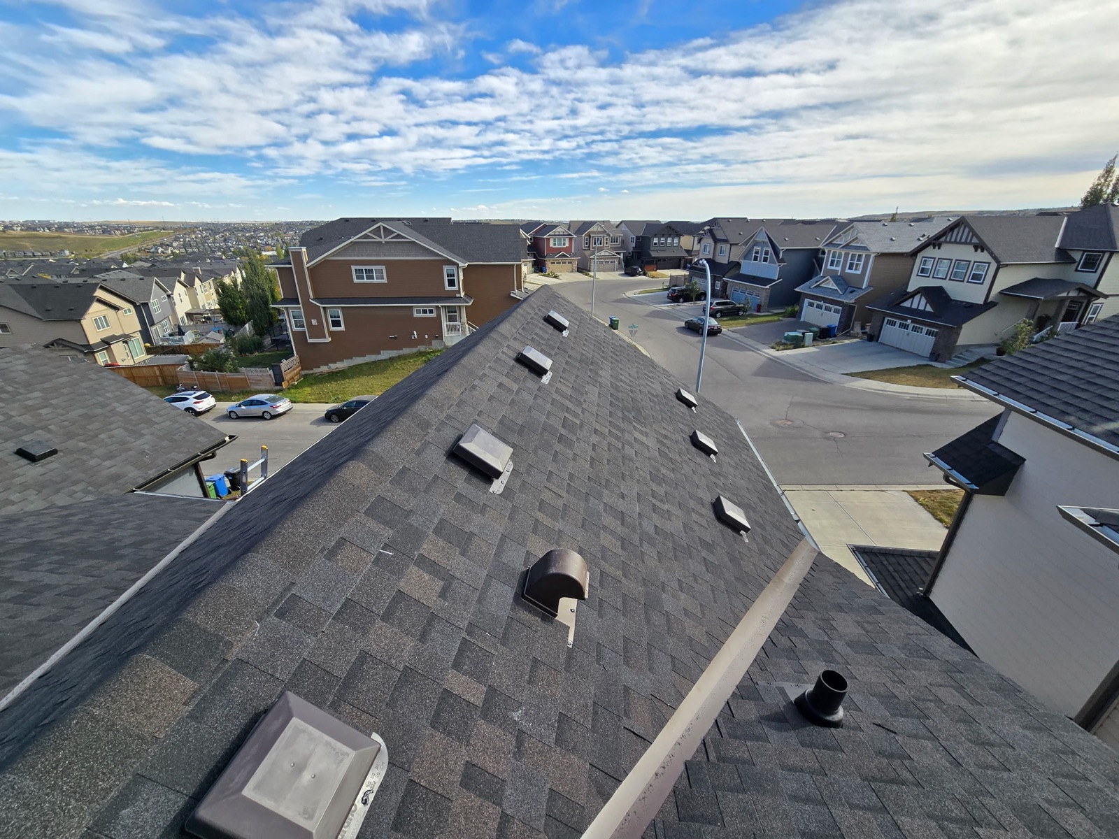 Brown shingle roof with vents, houses beyond