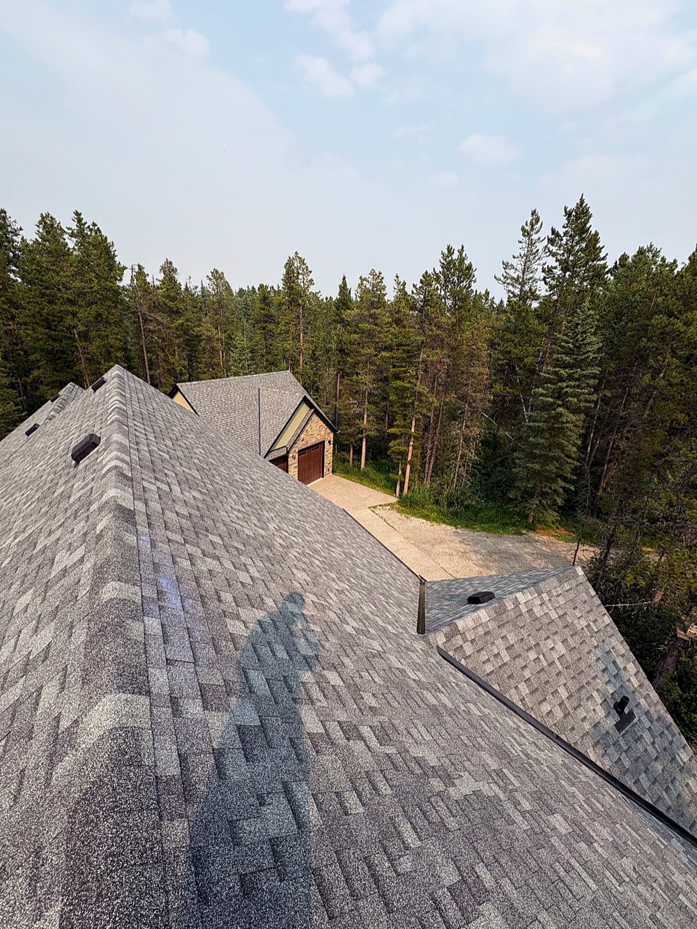 Grey shingles on a house roof with a matching detached garage and gravel drive below
